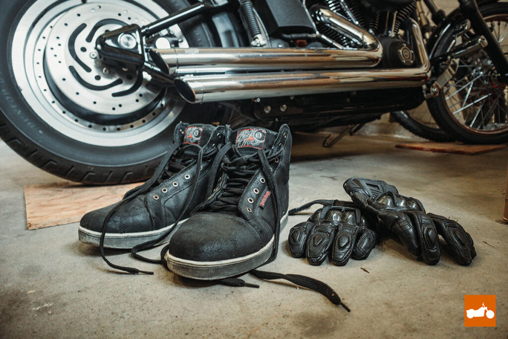 Riding boots and gloves next to Harley Davidson